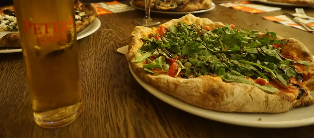 Pizza mit Rucola, Kirschtomaten und Balsamico neben einem frisch gezapften K&ouml;lsch
